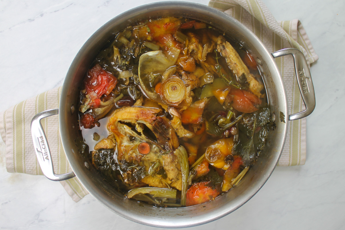 The pot of chicken stock with bones and veggies that is finished cooking ready to strain.