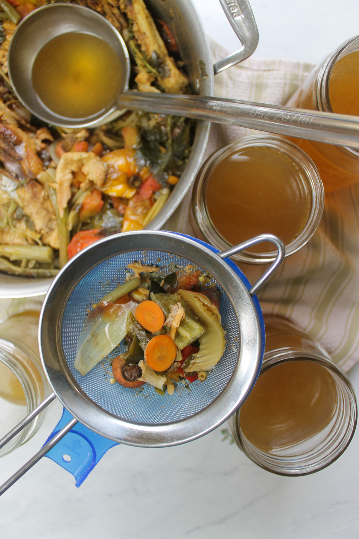 Straining chicken stock into jars using a jar funnel and fine mesh strainer.