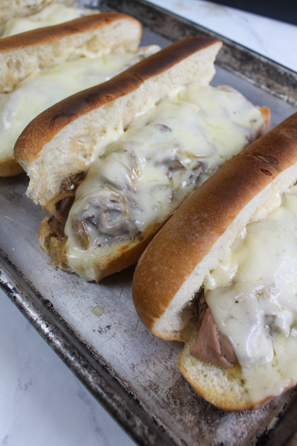 A sheet pan of melty, toasty French dip sandwiches from the oven.
