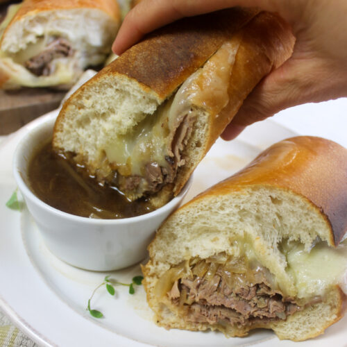 A French dip sandwich being dipped in au jus sauce.