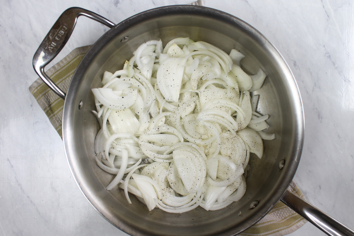 Sliced raw onions in a skillet ready to caramelized.