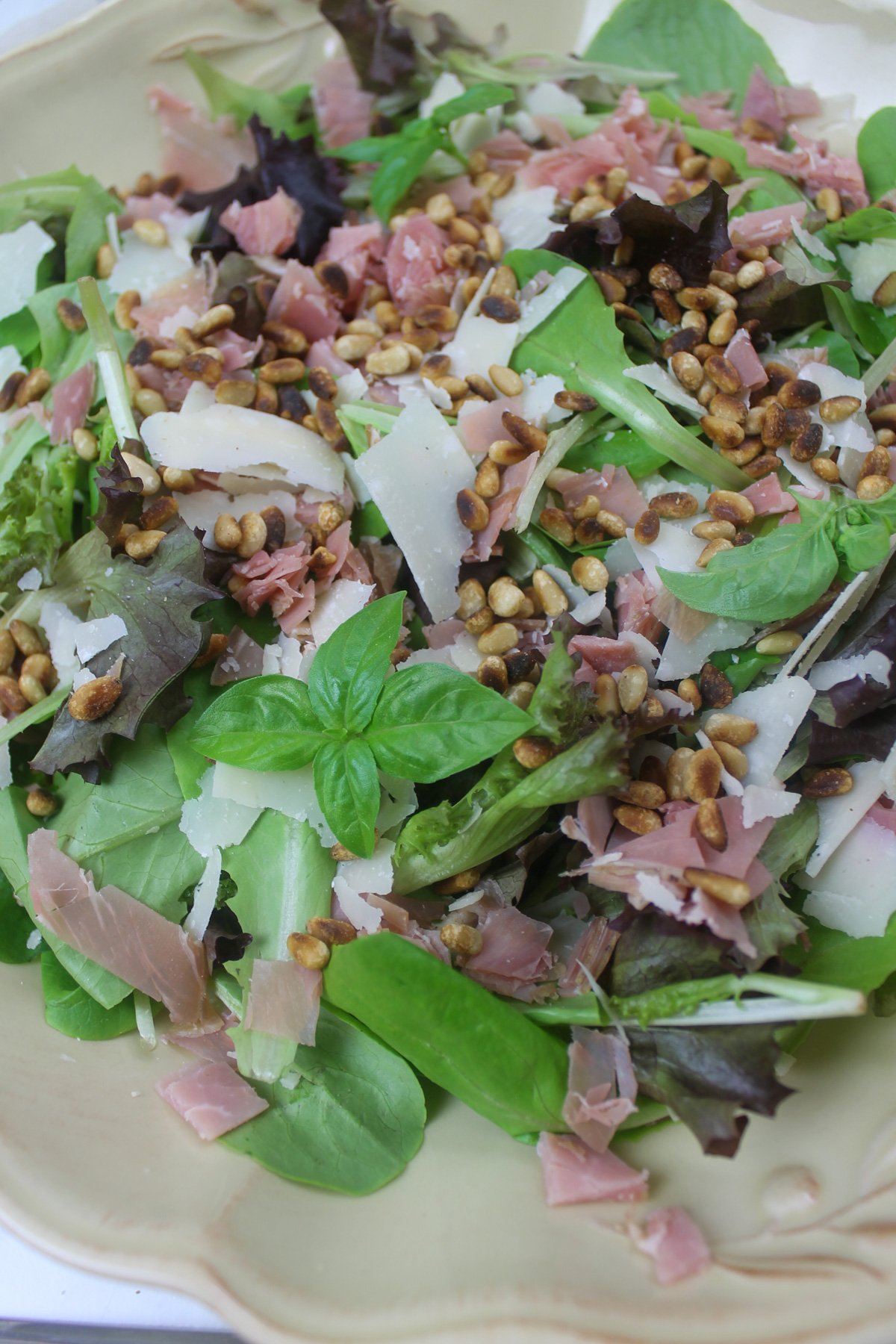 Salad platter with lettuce, prosciutto, Parmesan cheese and pine nuts.