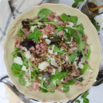 A salad platter with prosciutto and Parmesan cheese and a jar of basil vinaigrette.