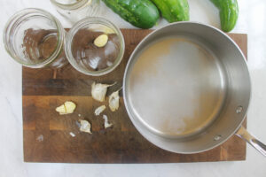 Preparing the brine in a saucepan and adding garlic and black peppercorns to jars.