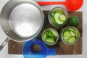Adding sliced cucumbers to 3 jars.