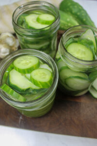 Top down view of refrigerator pickles in jars on a cutting board.