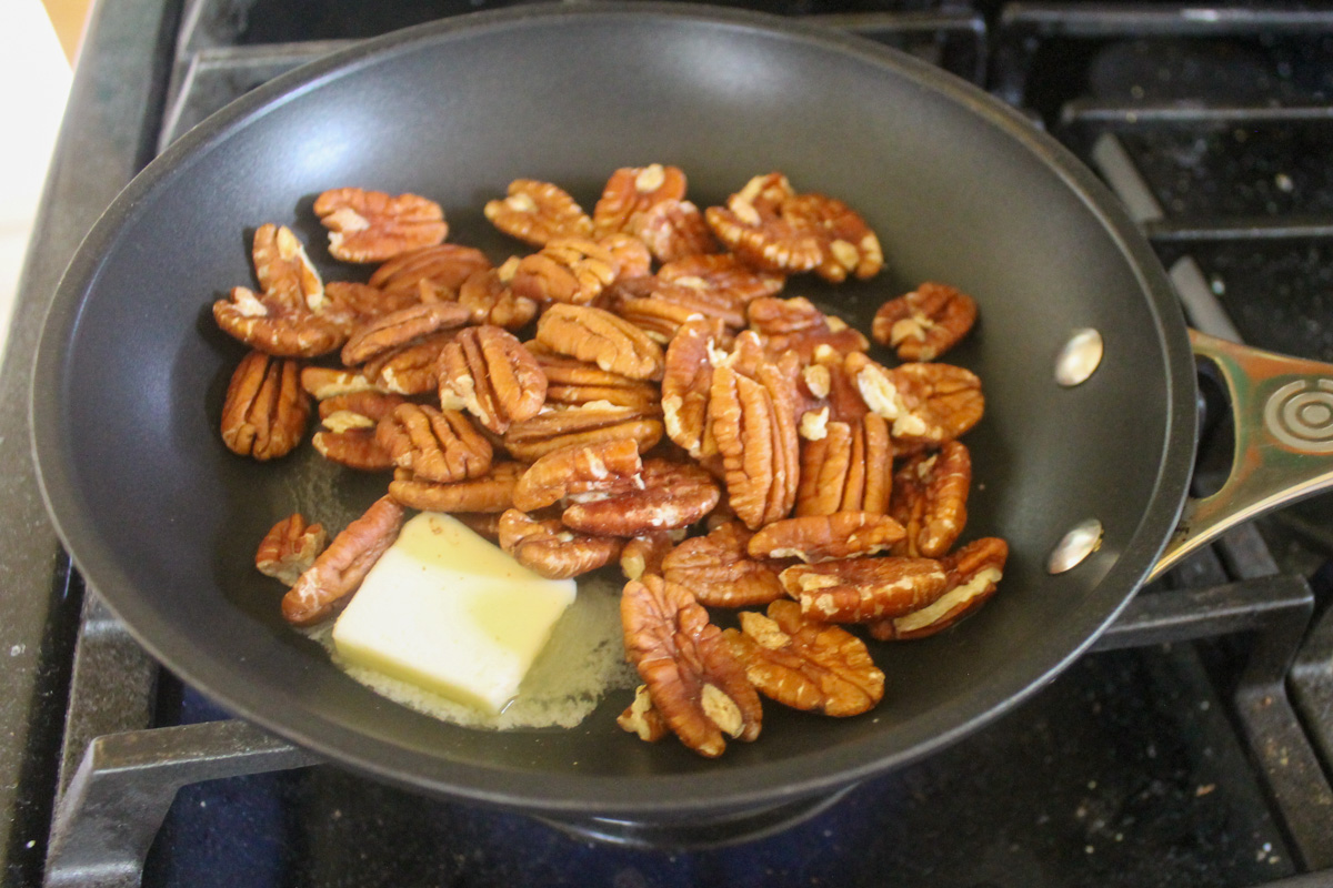 A skillet making candied pecans from raw nuts with butter and brown sugar.