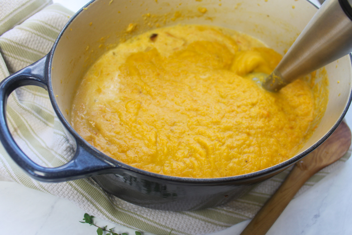 Pureeing butternut squash carrot soup with a stick blender.