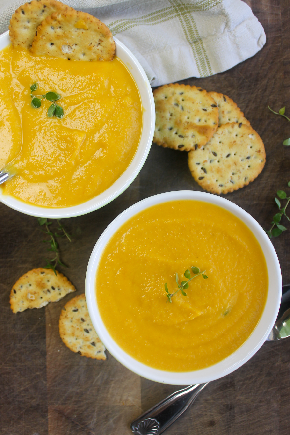 Bowls of butternut squash carrot soup on a dark wooden cutting board.