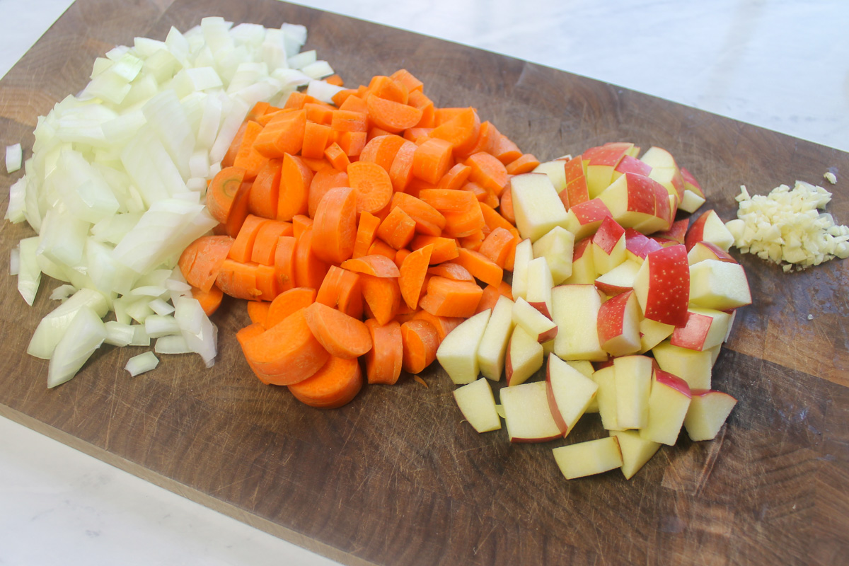 Chopped onions, carrots, apple and garlic on a cutting board.