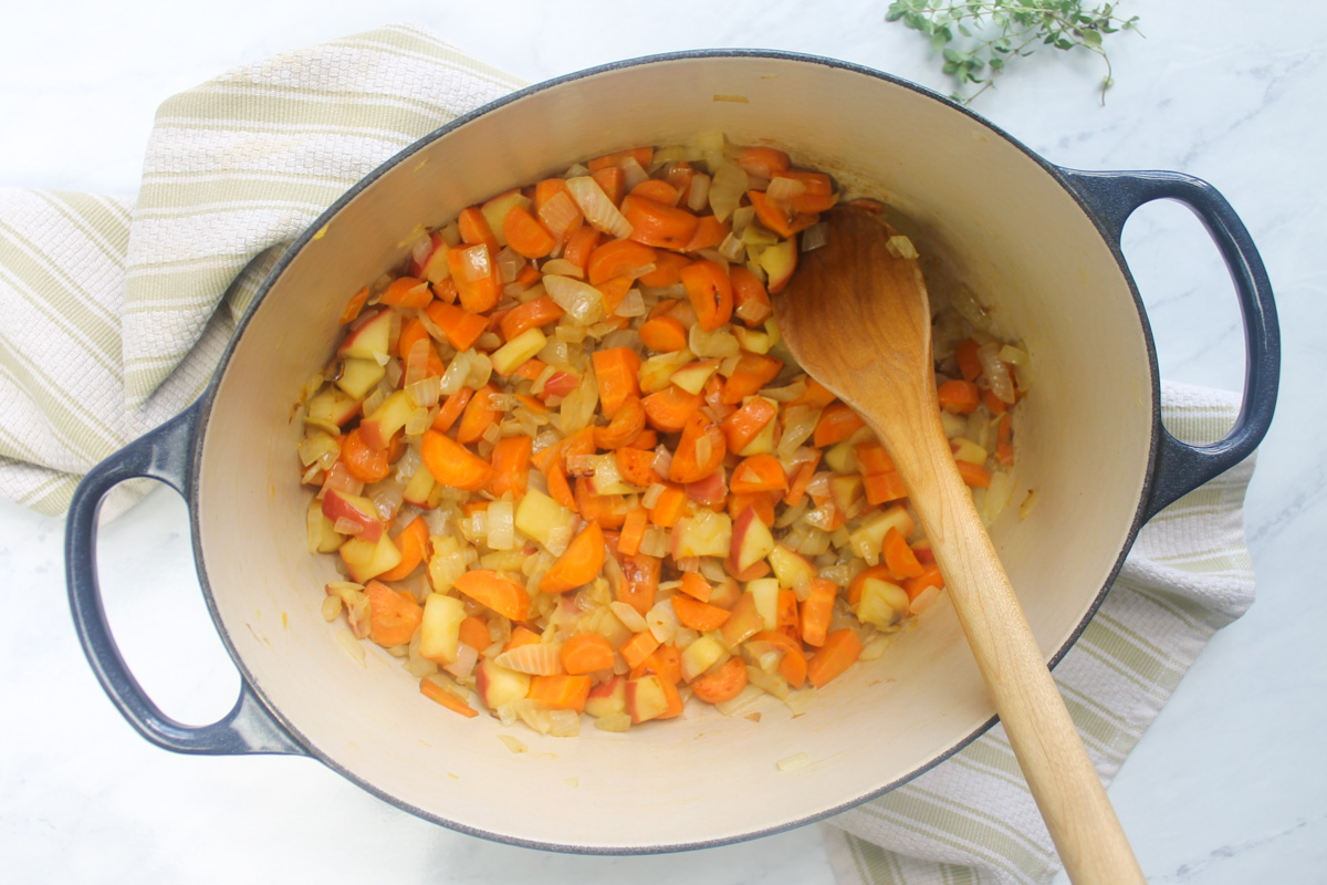 Sautéing onion, carrots, and apples in a soup pot.