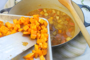 Scraping the roasted squash from the sheet pan into the pot of soup.