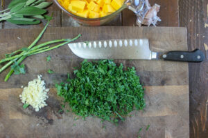 Chopped kale, minced garlic and butternut squash prepped on a cutting board.