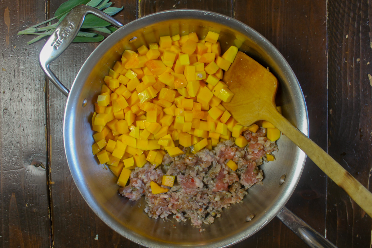 Cooking butternut squash and sausage in a skillet to start the sage cream sauce for butternut squash ravioli.