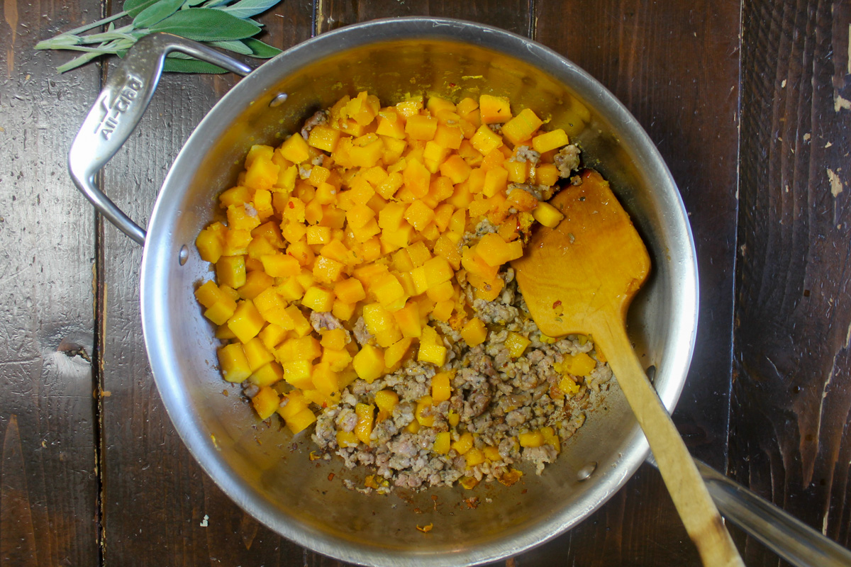 A skillet with browned sausage on half and sautéed butternut squash cubes.