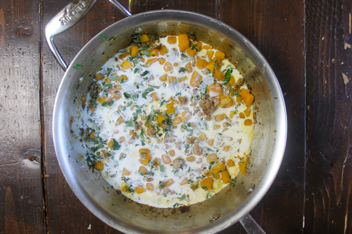 Adding cream to butternut squash and kale pasta.