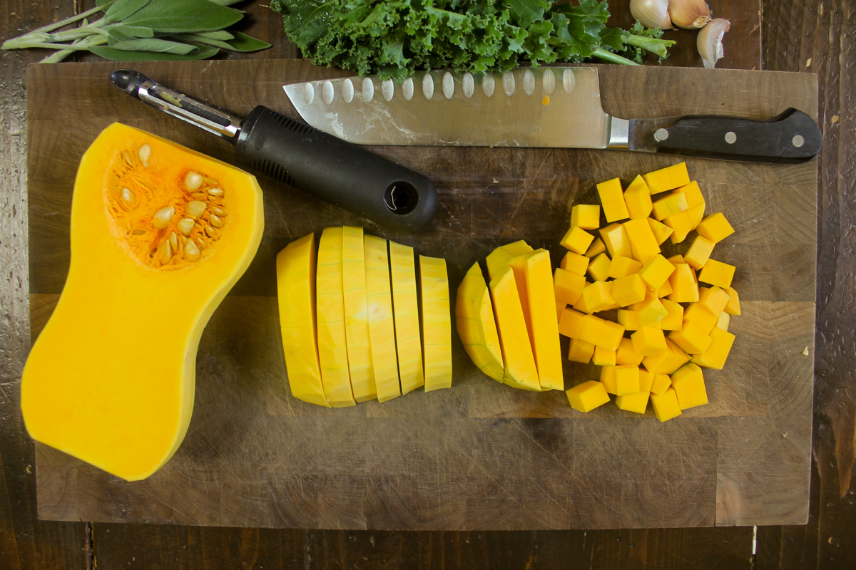 Chopping butternut squash into small cubes on a cutting board.