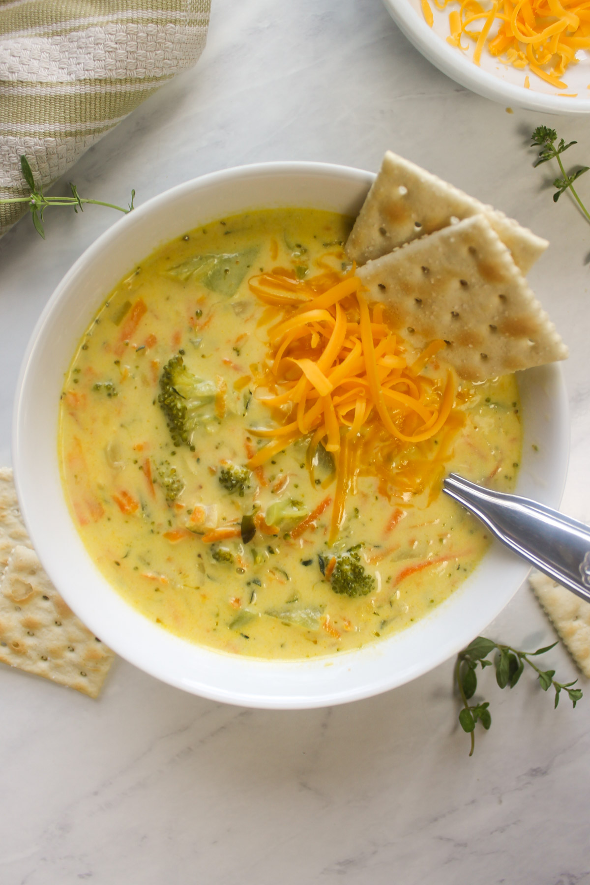 A bowl of broccoli zucchini soup with shredded cheddar cheese and crackers.