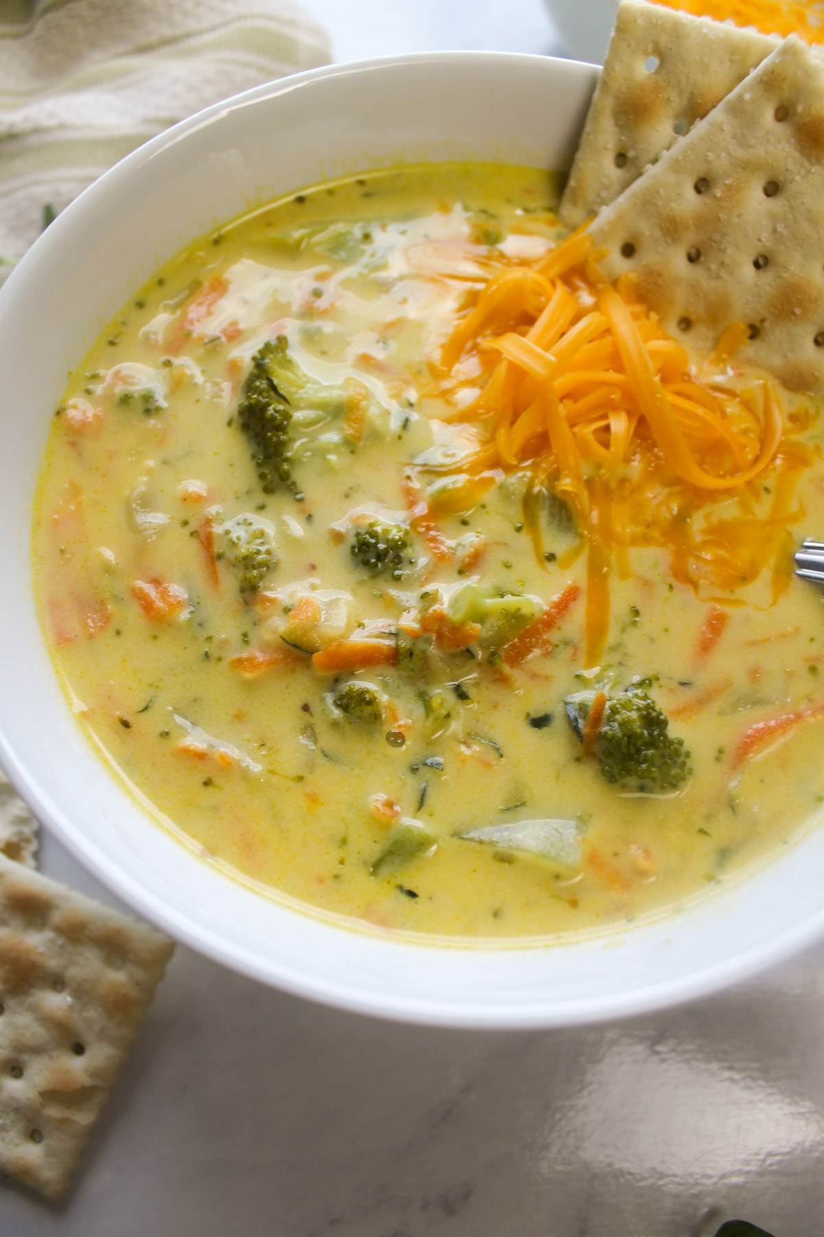 A bowl of carrots and broccoli soup with saltine crackers.