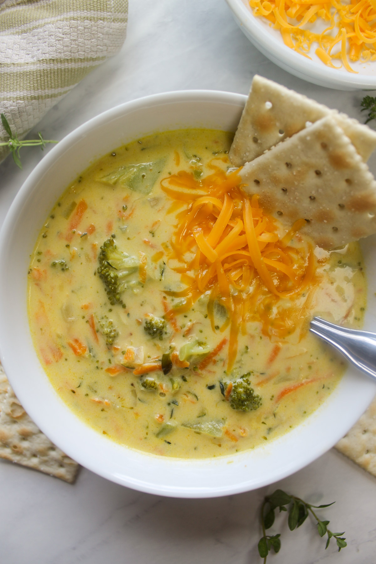 A white bowl of broccoli zucchini soup with extra cheese for serving.