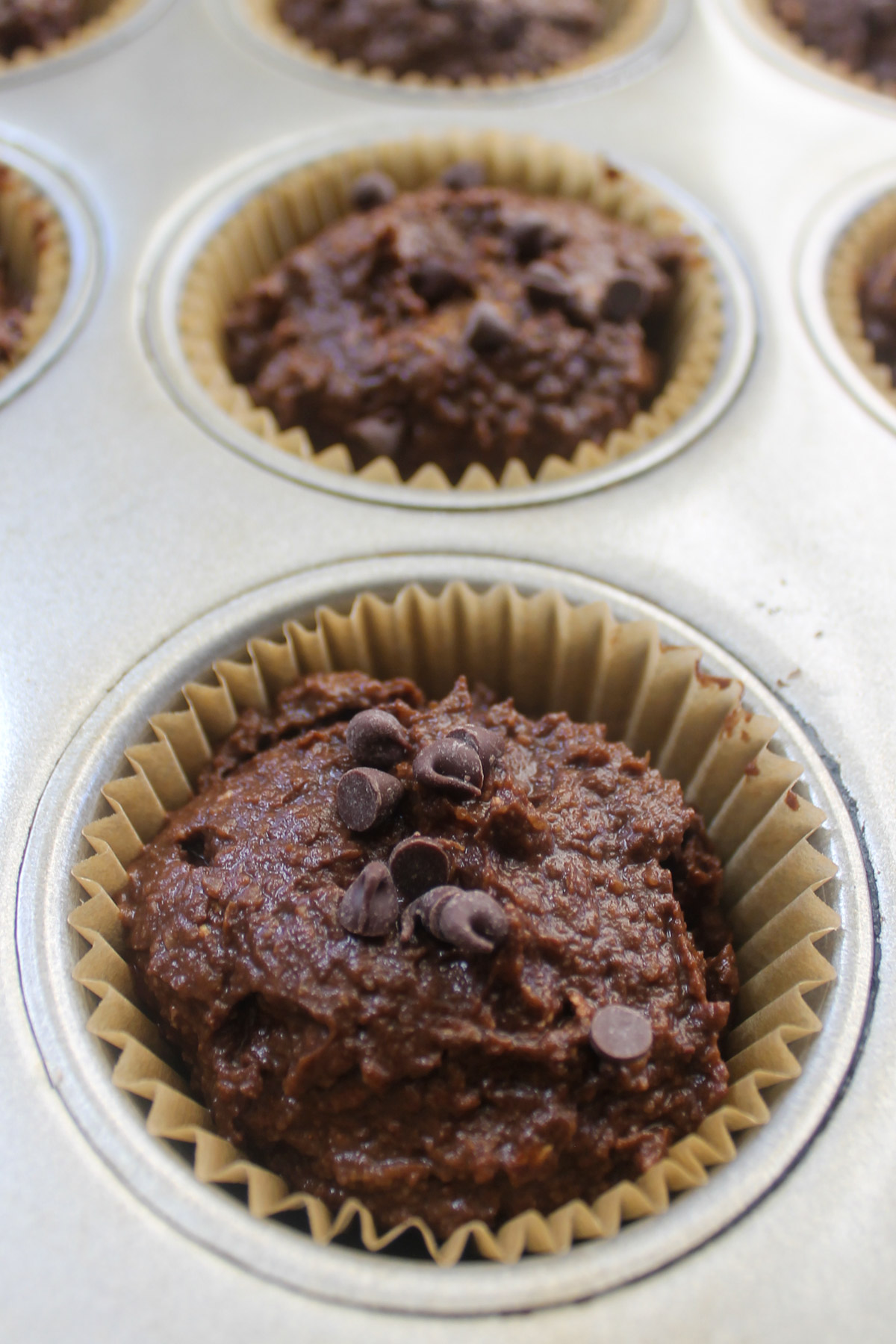 A close up of a filled muffin cup of batter, topped with chocolate chips.