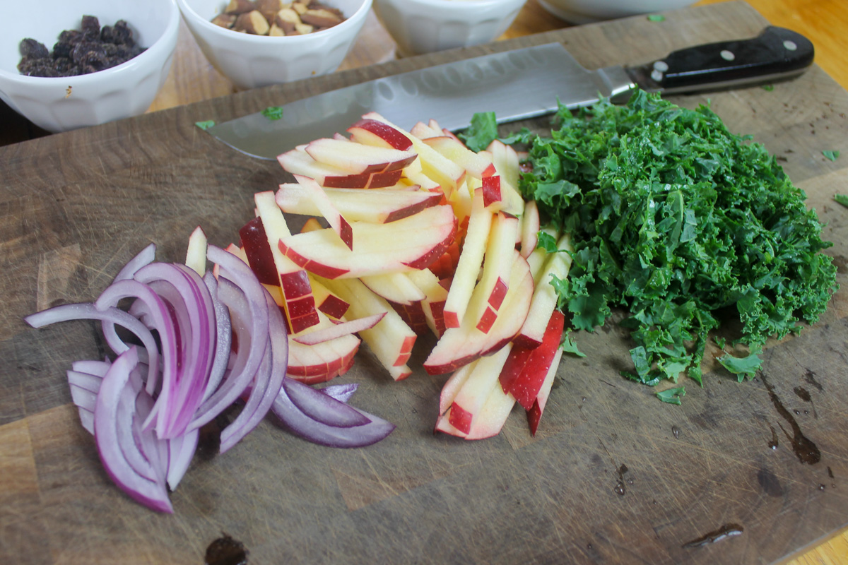 Slice kale, red onion and julienne apples on a cutting board.