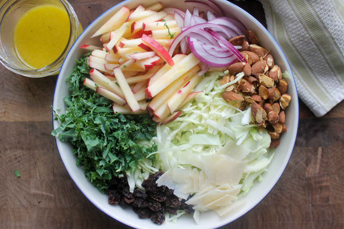 Adding all ingredients to a bowl of kale apple slaw.