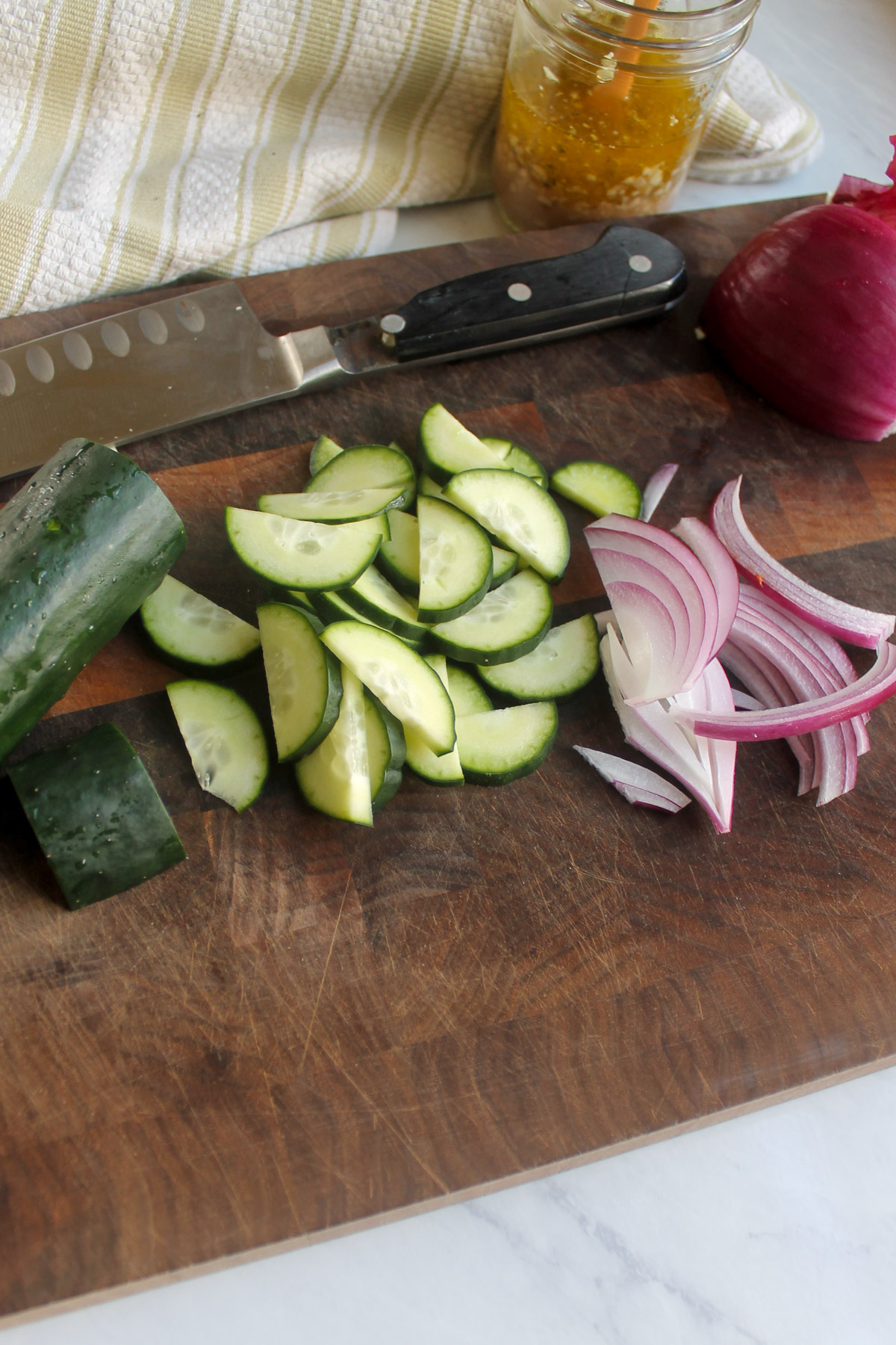 Sliced red onion and cucumbers on a cutting board.
