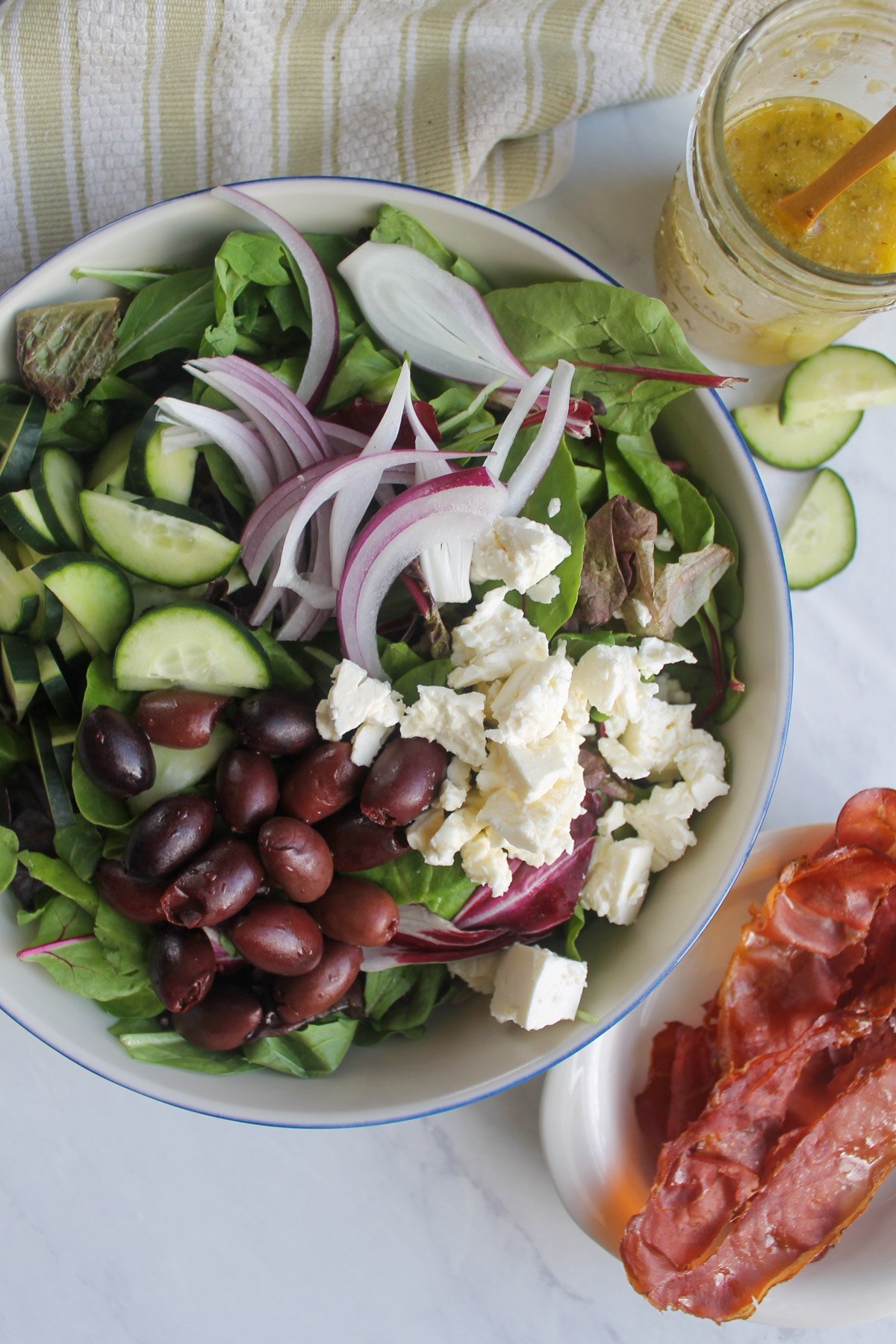 Italian salad assembled with mixed greens, cucumber, red onion, feta and kalamata olives piled on.