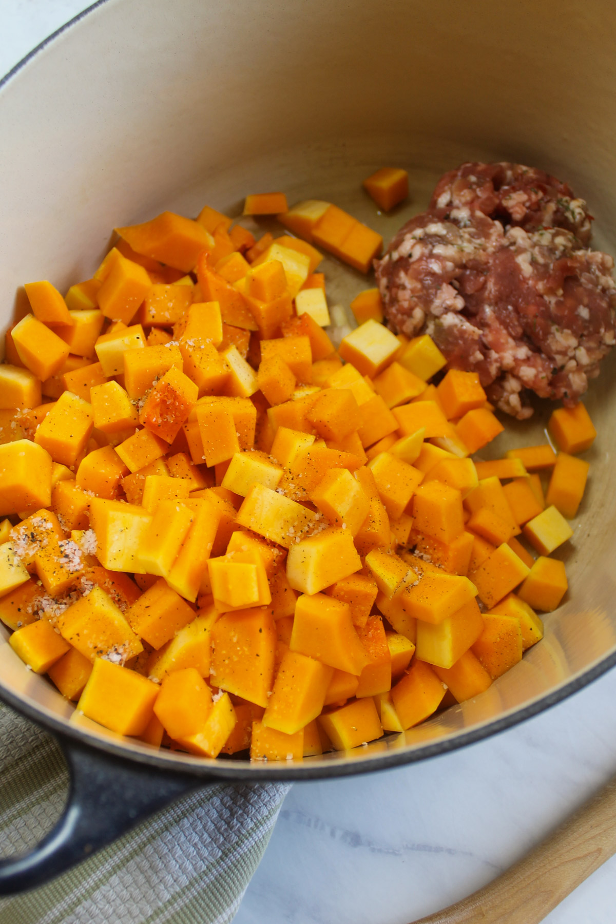 A soup pot started with the raw sausage on one side and onion and butternut squash on the other.