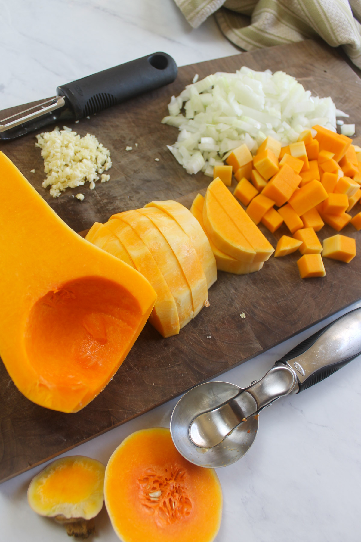 Chopping butternut squash, onion and garlic on a cutting board.