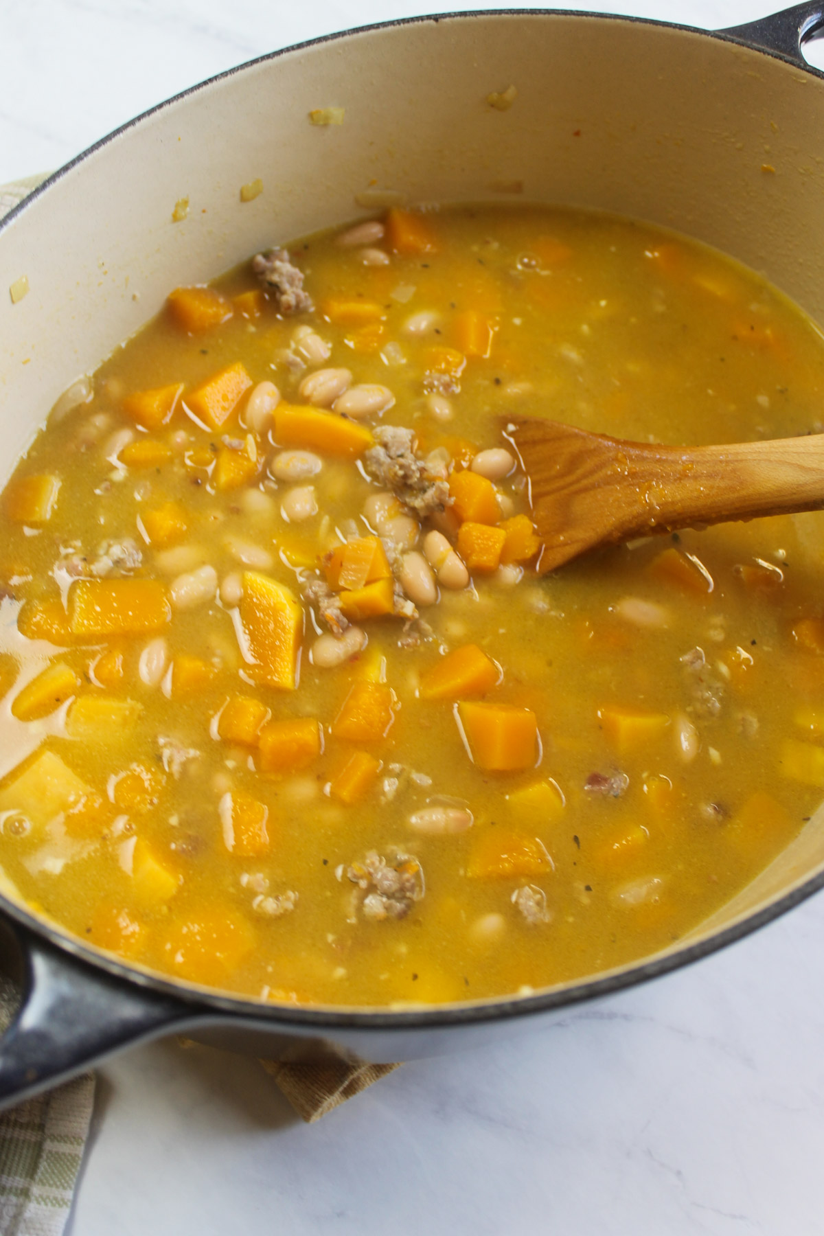 Adding the stock, beans and orzo to the pot of soup.