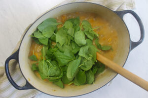 Adding handfuls of raw spinach to wilt into the soup pot.