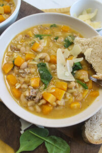 A bowl of Italian sausage butternut squash soup with spinach and crusty bread.