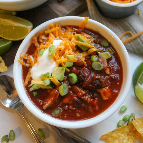 A bowl of turkey chili topped with cheese, green onions, sour cream and avocado.