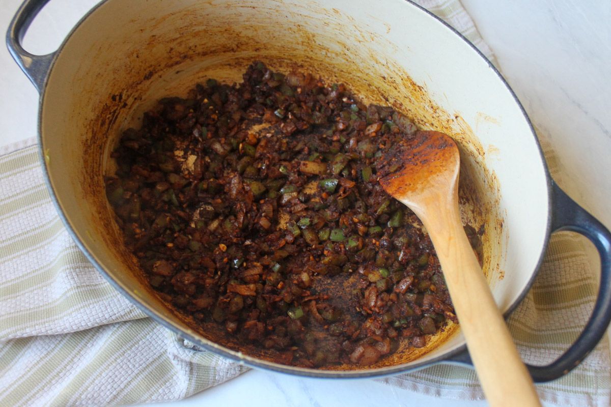 Cooking the onion and green pepper with the spices until toasted and dark brown in color.