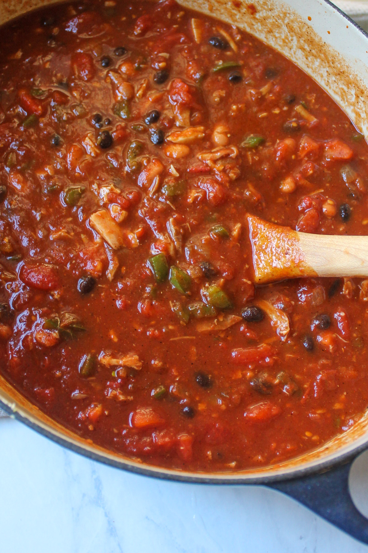 A pot of turkey chili with bits of green pepper, black beans, pinto beans and shredded turkey.