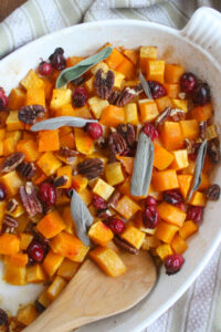 A white dish of maple roasted butternut squash with fresh cranberries.
