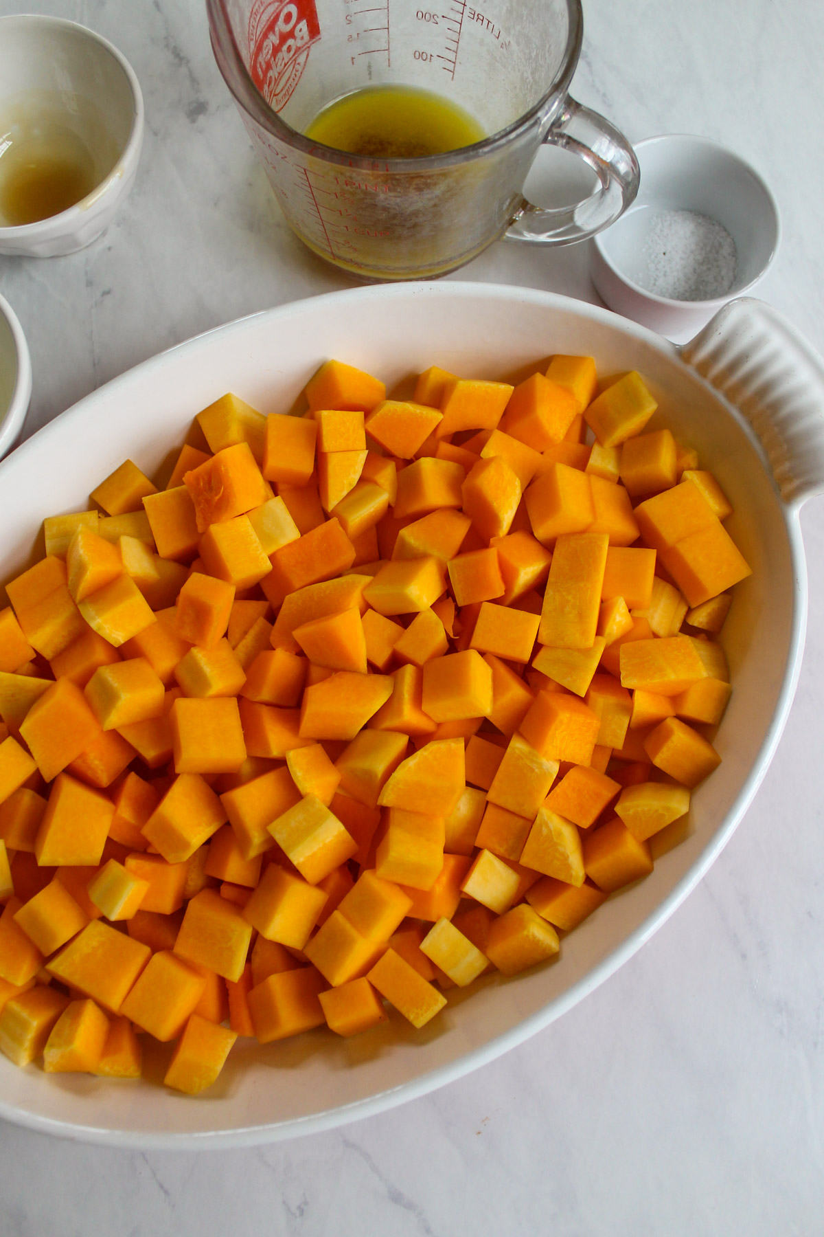 Butternut squash peeled and chopped and added to a white baking dish.