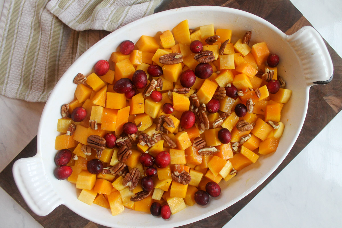 Adding the cranberries and pecans to the par-baked butternut squash.