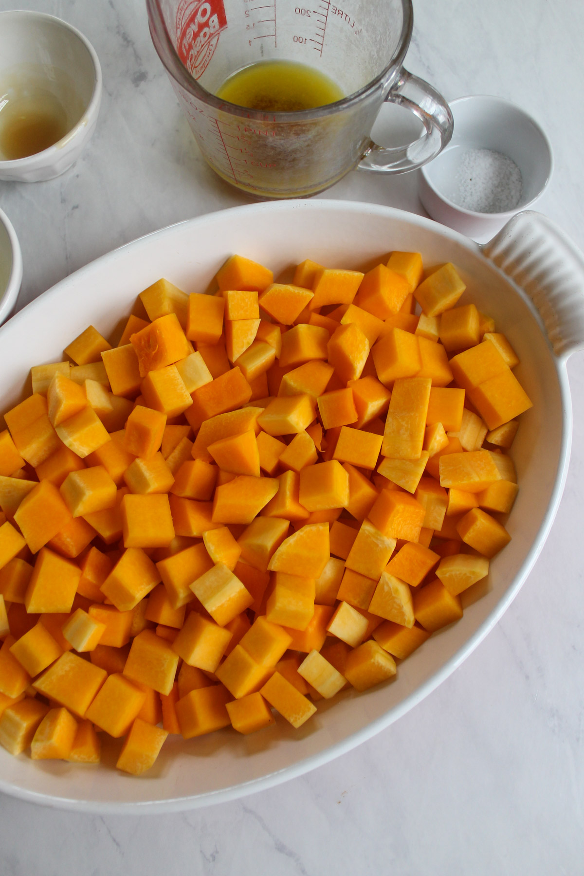 Butternut squash peeled and chopped and added to a white baking dish.