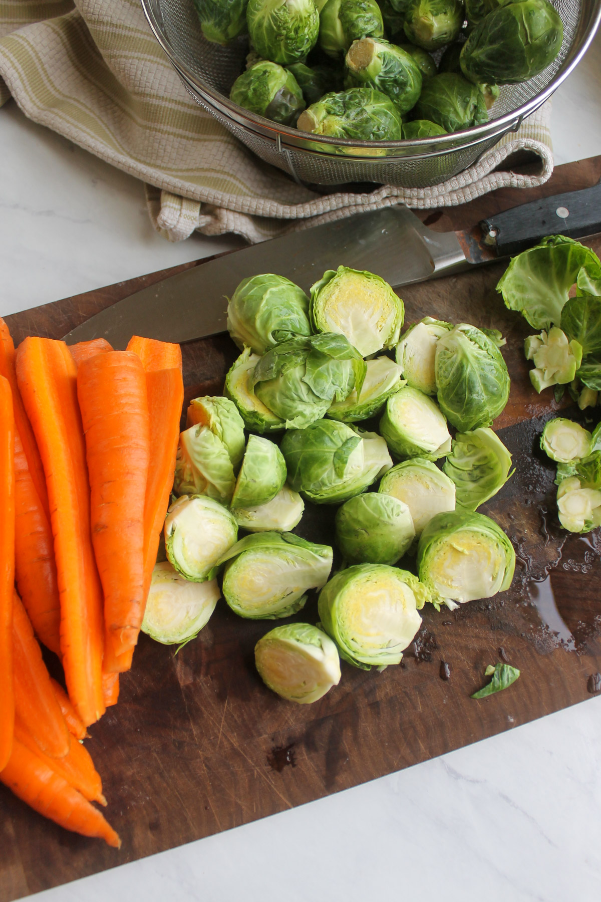 Trimming and slices carrots and Brussel sprouts on a cutting board.