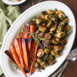 Roasted carrots and Brussel sprouts on a large white platter for a holiday side dish.