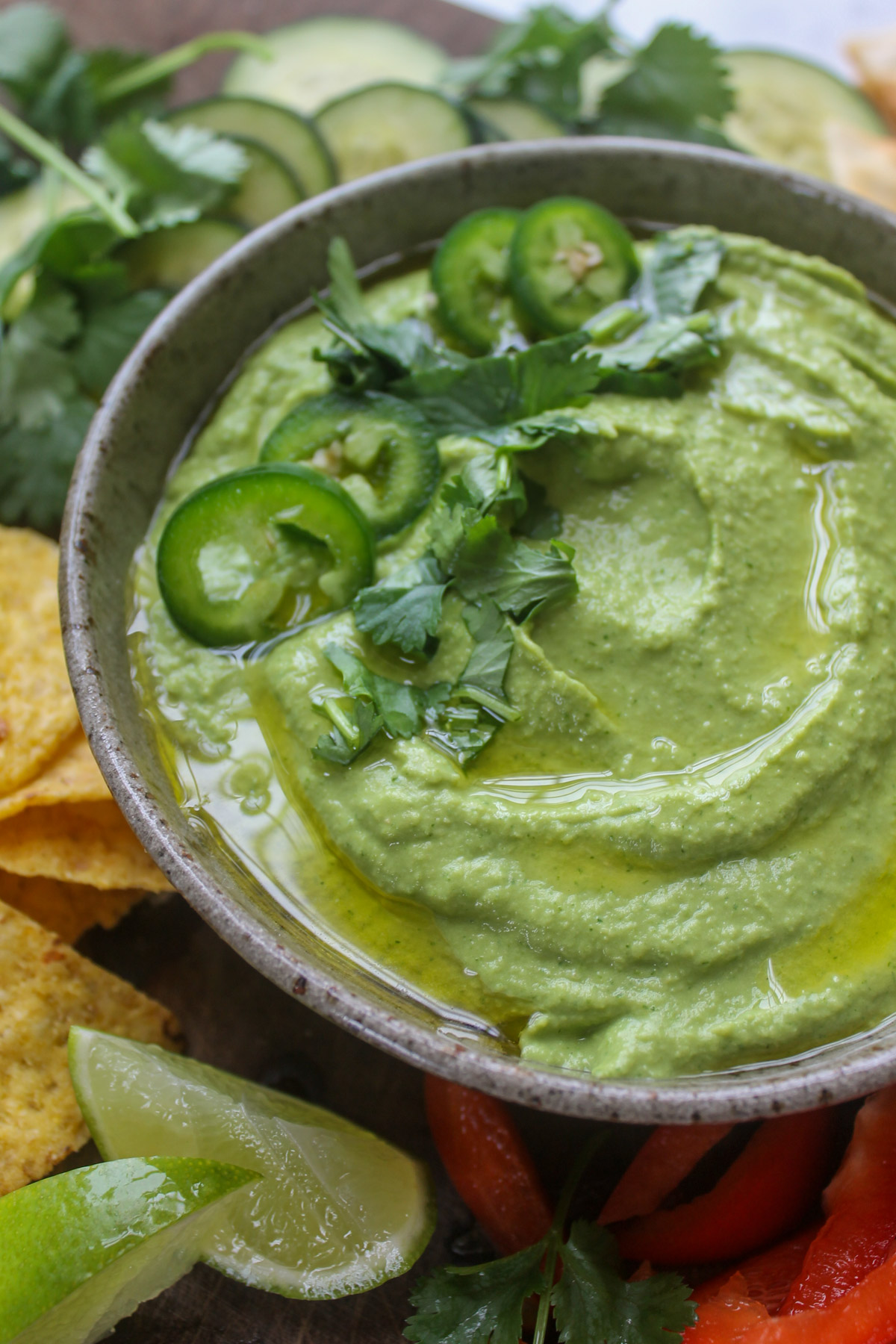 A bowl of cilantro jalapeño hummus with lime wedges and snacks for dipping.