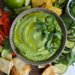 Cilantro lime hummus drizzled with olive oil and garnished with fresh herbs and jalapeño pepper slices.