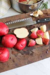 Chopping red potatoes on a cutting board and adding to a pot of water.