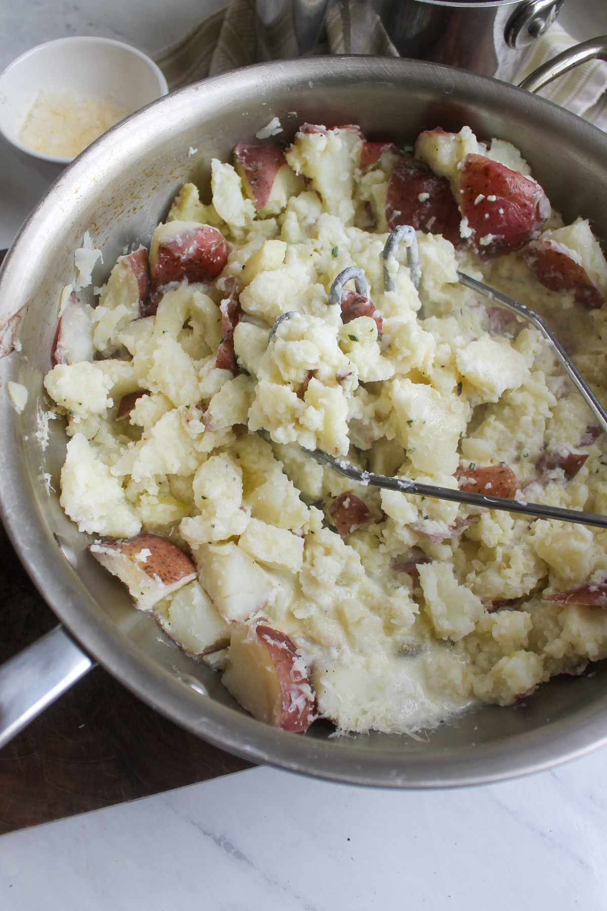 Mashing red potatoes in a large pot with a potato masher.