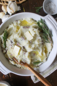 A serving bowl of mashed potatoes with fresh rosemary sprigs.