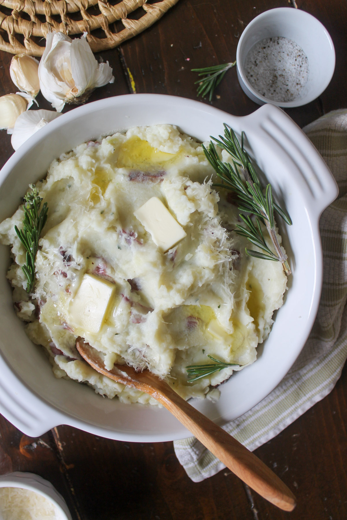 A white bowl of rosemary garlic mashed potatoes with a wooden spoon.