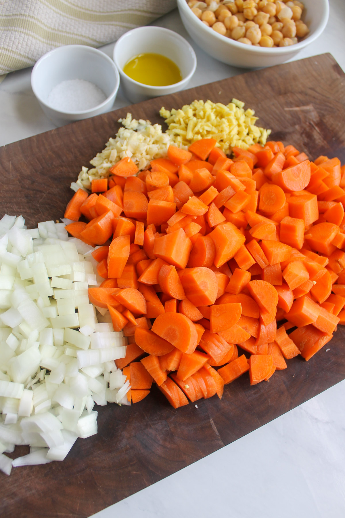 A cutting board with chopped onion, carrots, garlic and ginger for soup.